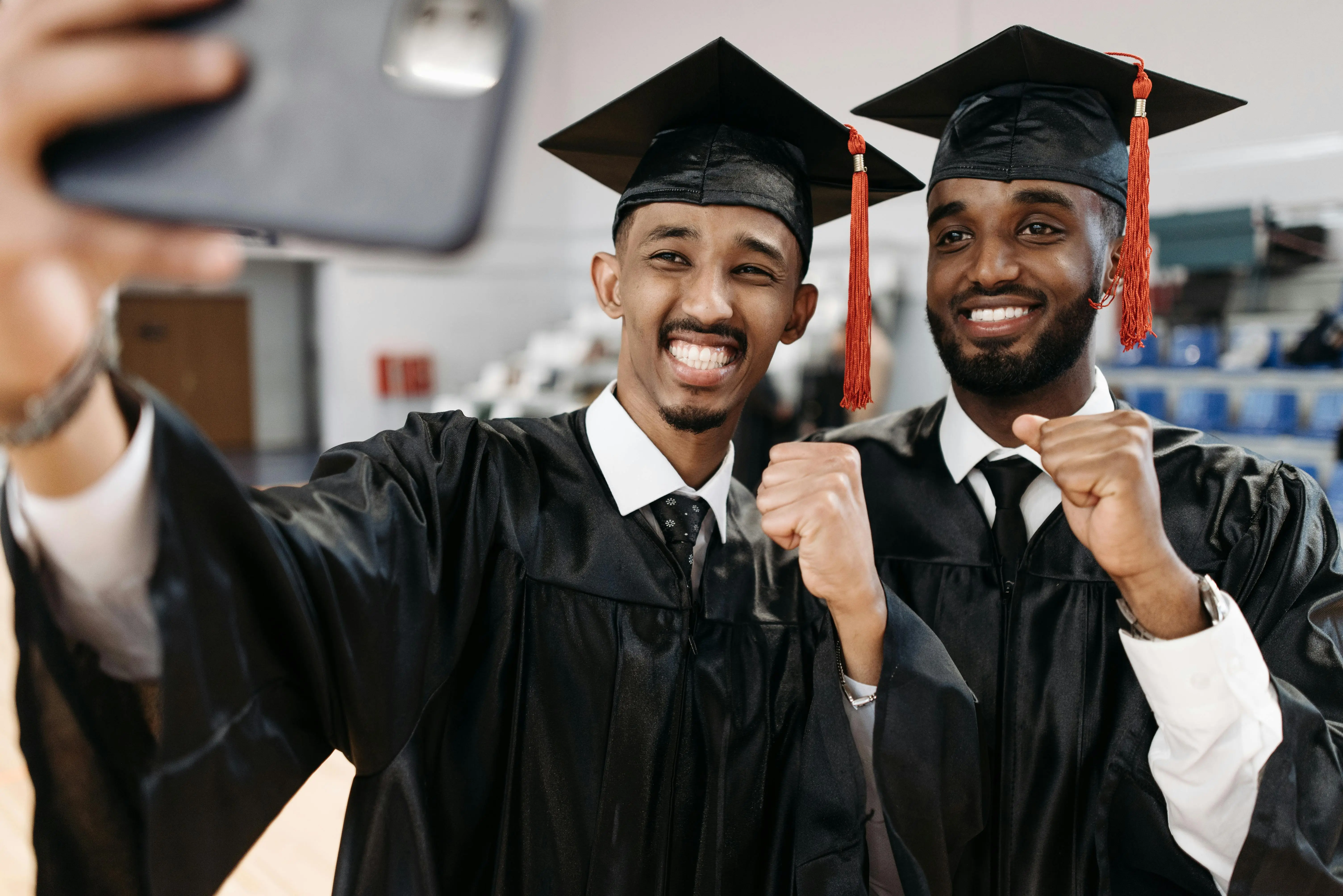 2 men in graduation cap and gowns, taking a picture to celebrate their achievement